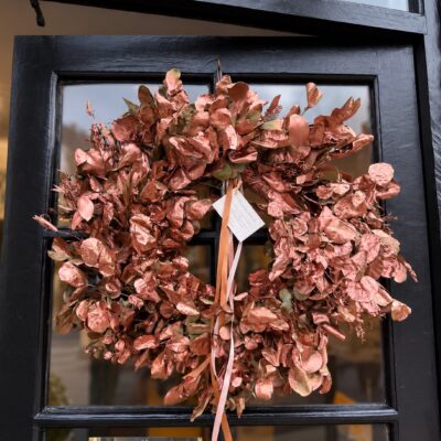 Handmade copper and rose-gold dried foliage wreath with trailing ribbons on a dark door