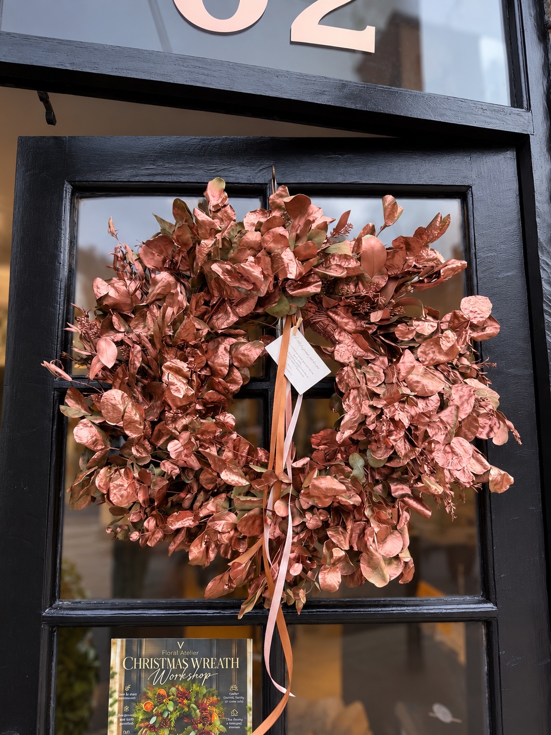 Handmade copper and rose-gold dried foliage wreath with trailing ribbons on a dark door